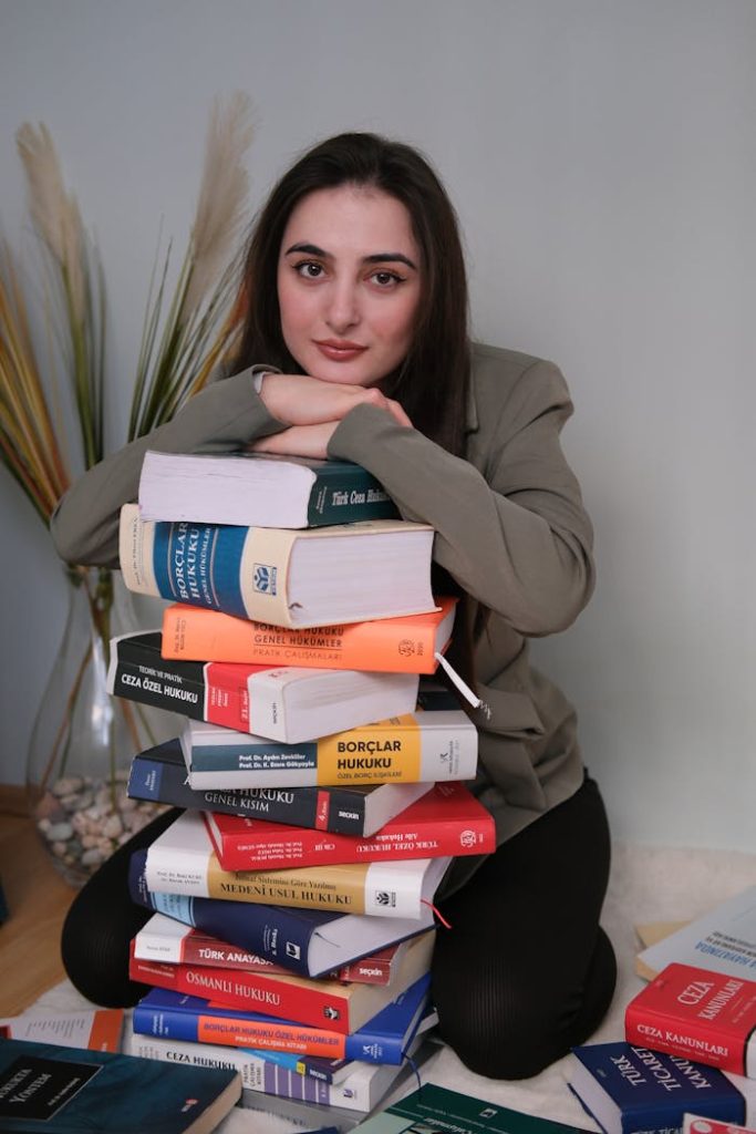 A woman poses confidently with a stack of law books in a studio setting, emphasizing education and legal studies.