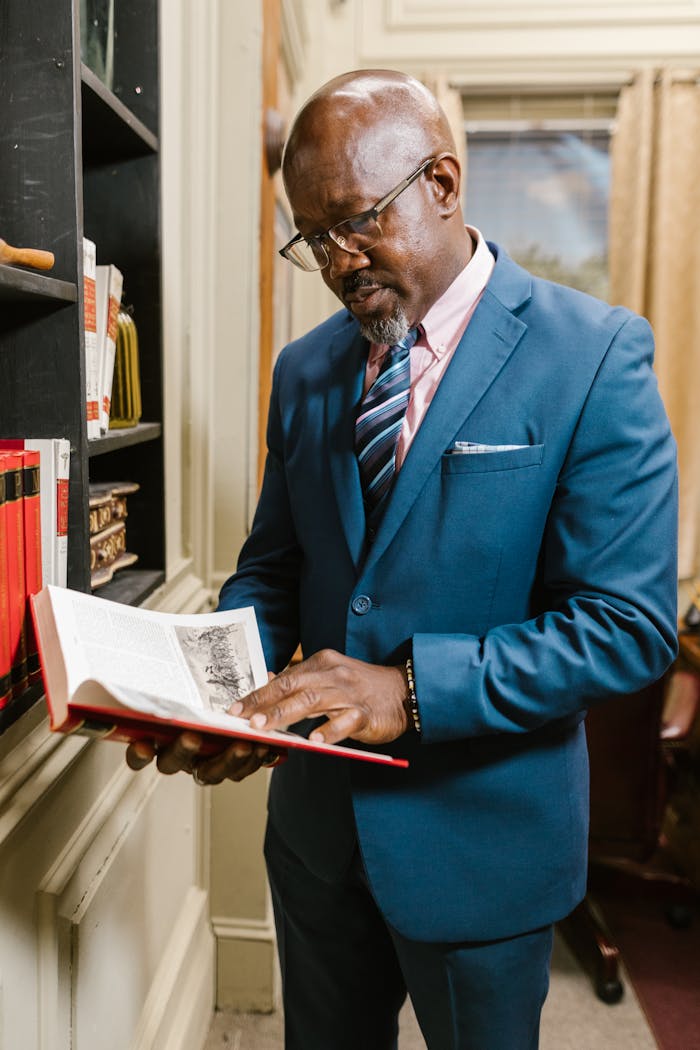 Mature businessman in a suit reads a book in an office setting, focused and thoughtful.